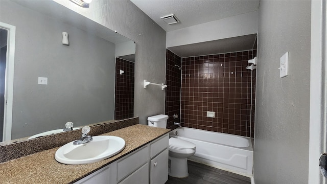 full bathroom featuring vanity, tiled shower / bath combo, toilet, a textured ceiling, and wood-type flooring