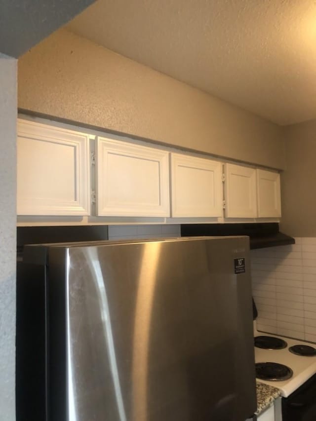 details with stainless steel fridge, backsplash, white cabinetry, and white stovetop