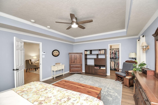 bedroom with ceiling fan, light hardwood / wood-style floors, a walk in closet, a closet, and ornamental molding