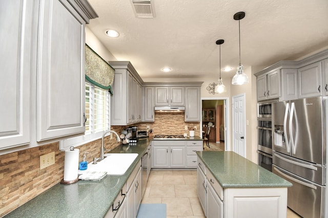 kitchen with appliances with stainless steel finishes, backsplash, gray cabinetry, sink, and a kitchen island