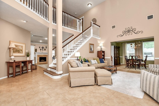 living room featuring light tile patterned floors, a towering ceiling, a notable chandelier, and a tiled fireplace