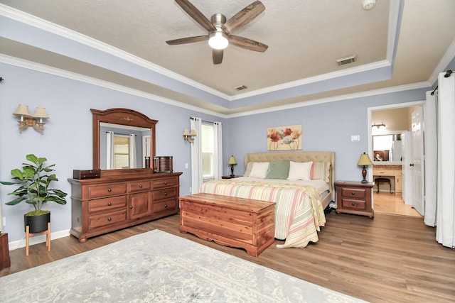 bedroom with ornamental molding, a raised ceiling, ceiling fan, hardwood / wood-style floors, and connected bathroom