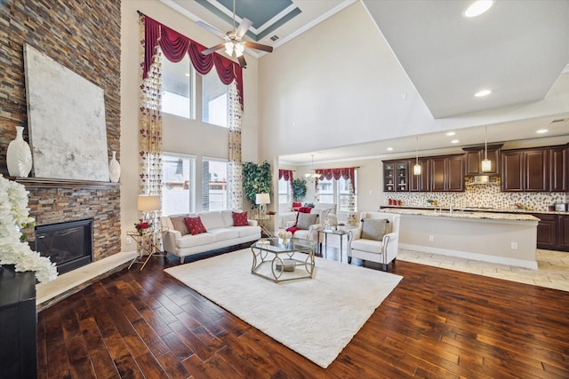 living room with a towering ceiling, ceiling fan with notable chandelier, dark hardwood / wood-style flooring, and a fireplace