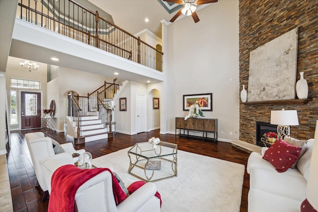 living room featuring a high ceiling, dark wood-type flooring, ceiling fan with notable chandelier, and a fireplace