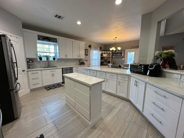 kitchen with stainless steel appliances, sink, pendant lighting, an inviting chandelier, and white cabinets