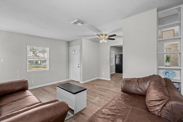 living room with ceiling fan, a textured ceiling, and light hardwood / wood-style flooring