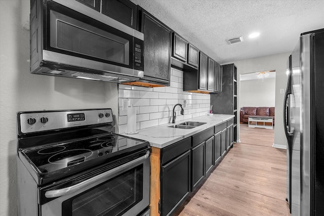 kitchen featuring light stone counters, a textured ceiling, stainless steel appliances, sink, and light hardwood / wood-style floors