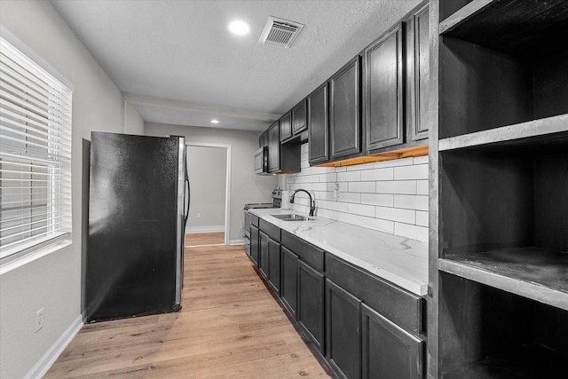 kitchen featuring sink, electric stove, decorative backsplash, black refrigerator, and light wood-type flooring