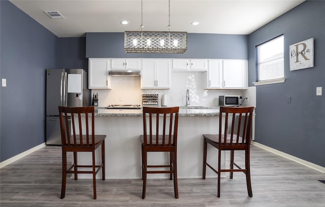 kitchen with light stone countertops, appliances with stainless steel finishes, a kitchen breakfast bar, white cabinets, and dark hardwood / wood-style floors