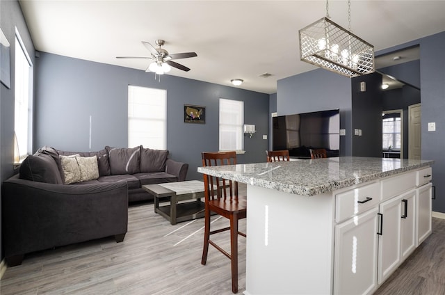 kitchen with pendant lighting, a center island, white cabinets, a kitchen breakfast bar, and light wood-type flooring