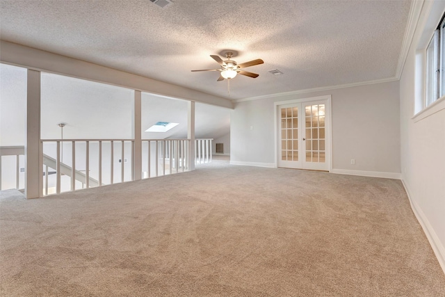 carpeted spare room featuring ceiling fan, vaulted ceiling with skylight, a textured ceiling, and ornamental molding