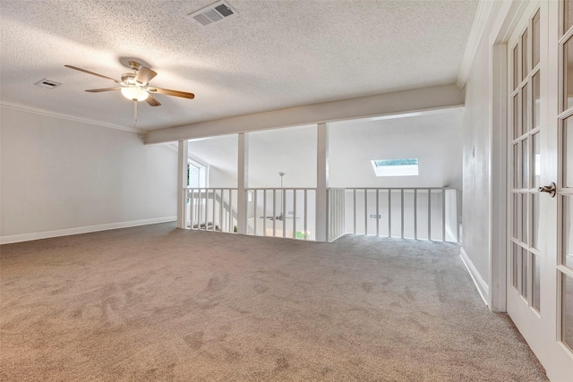 carpeted empty room featuring ceiling fan, crown molding, a skylight, and a textured ceiling