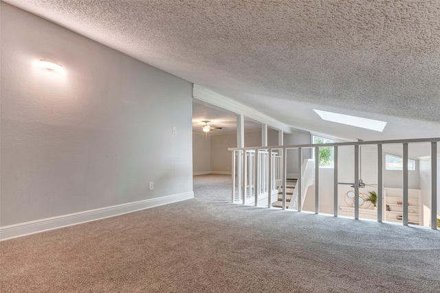 carpeted spare room featuring a textured ceiling, ceiling fan, and lofted ceiling with skylight