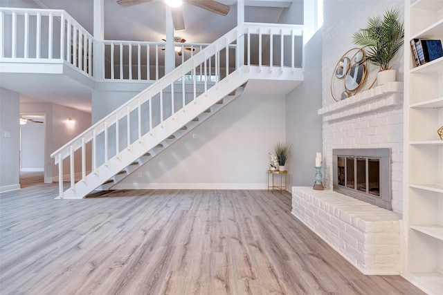 unfurnished living room featuring ceiling fan, a fireplace, a high ceiling, and light hardwood / wood-style floors