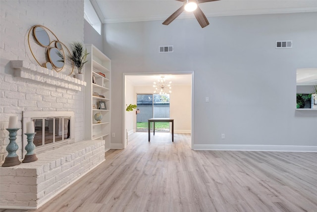 unfurnished living room with light wood-type flooring, ceiling fan with notable chandelier, a fireplace, and a high ceiling