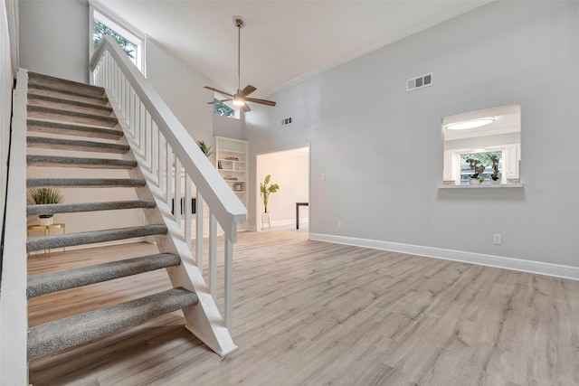 staircase with ceiling fan, hardwood / wood-style floors, crown molding, and a high ceiling