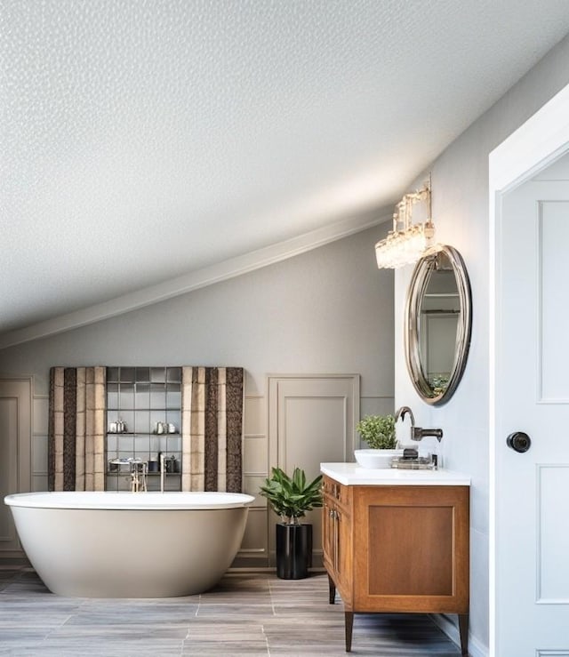 bathroom with vanity, a tub, vaulted ceiling, and a textured ceiling