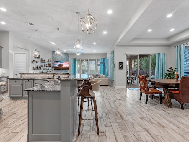 kitchen with pendant lighting, stone countertops, gray cabinetry, and light hardwood / wood-style floors