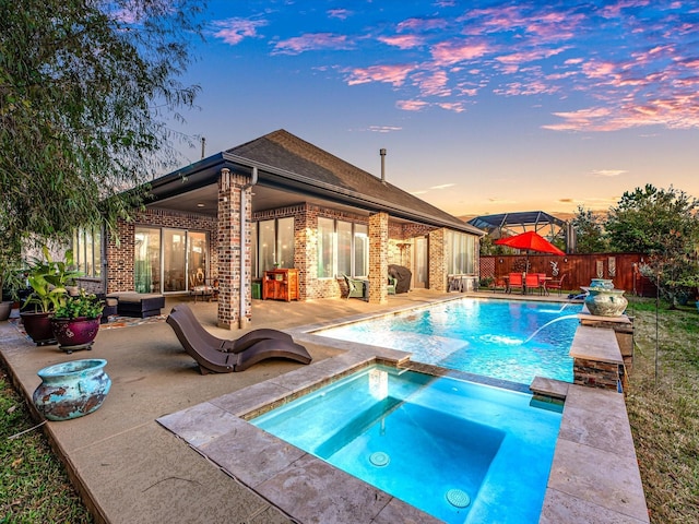 pool at dusk with pool water feature, an in ground hot tub, and a patio