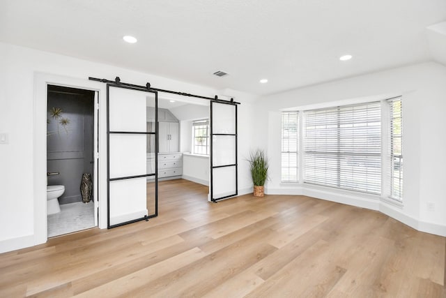 unfurnished bedroom with connected bathroom, a barn door, and light hardwood / wood-style flooring