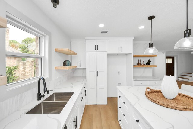 kitchen featuring white cabinetry, light hardwood / wood-style floors, decorative light fixtures, light stone counters, and sink