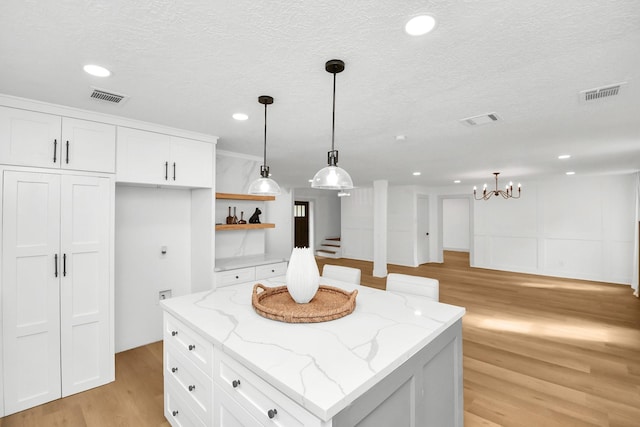 kitchen with light stone countertops, white cabinets, a kitchen island, light hardwood / wood-style floors, and hanging light fixtures