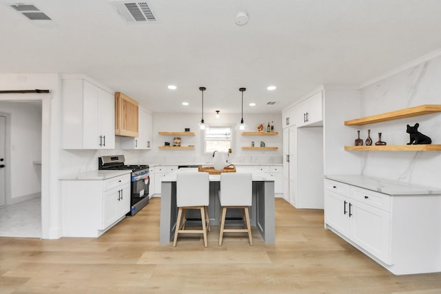 kitchen featuring white cabinetry, stainless steel gas range, a breakfast bar area, hanging light fixtures, and a center island