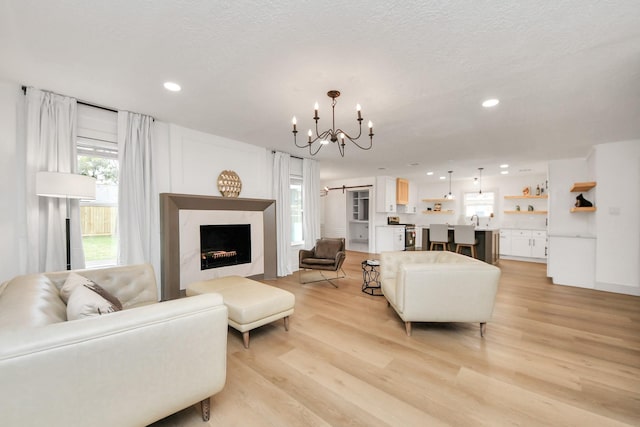 living room with sink, an inviting chandelier, a textured ceiling, and light hardwood / wood-style floors