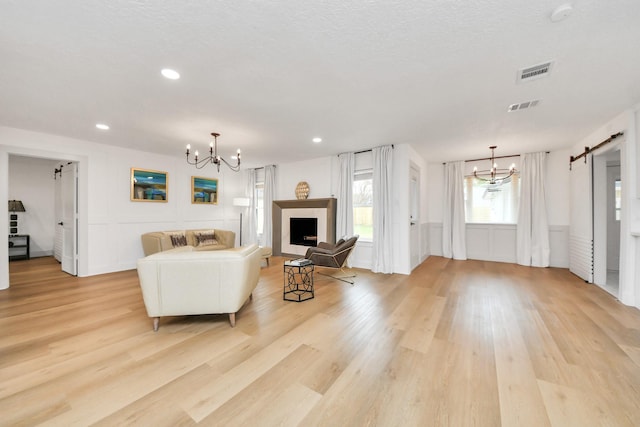 living room featuring a barn door, an inviting chandelier, a textured ceiling, and light hardwood / wood-style flooring