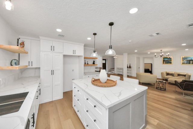 kitchen featuring a kitchen island, light hardwood / wood-style flooring, hanging light fixtures, light stone countertops, and white cabinets