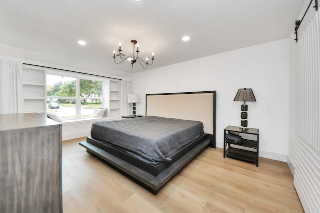 bedroom featuring a barn door, wood-type flooring, a chandelier, and a textured ceiling