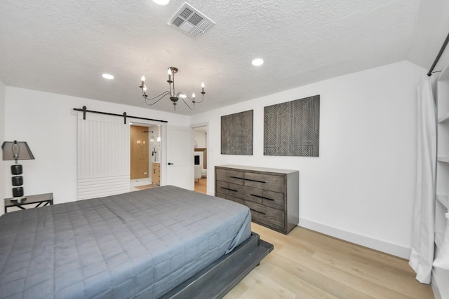 bedroom featuring a textured ceiling, an inviting chandelier, a barn door, and light hardwood / wood-style flooring