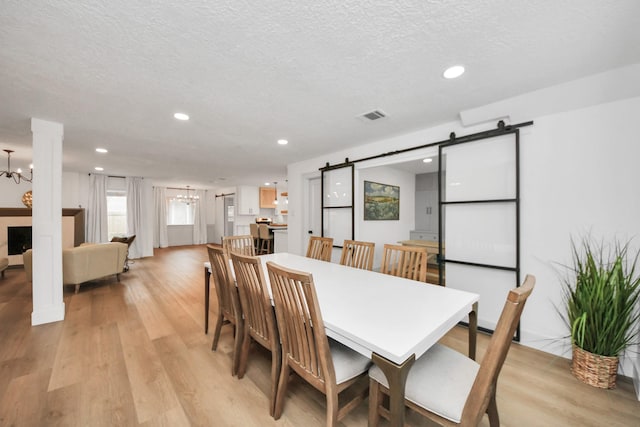 dining room with light hardwood / wood-style floors, a textured ceiling, a barn door, and an inviting chandelier