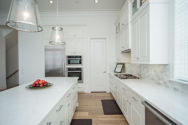 kitchen with appliances with stainless steel finishes, crown molding, decorative light fixtures, light hardwood / wood-style flooring, and white cabinetry