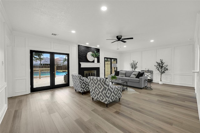 living room with french doors, ceiling fan, light wood-type flooring, a textured ceiling, and a fireplace