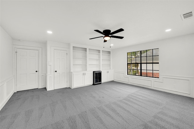 unfurnished living room featuring light carpet, built in shelves, wine cooler, and ceiling fan