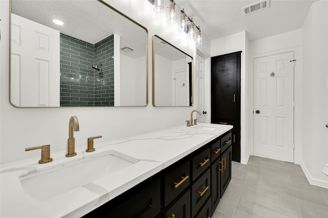 bathroom with tile patterned flooring, vanity, tiled shower, and a textured ceiling