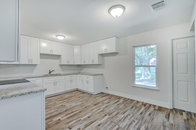 kitchen featuring light stone countertops, light wood-type flooring, white cabinetry, and sink