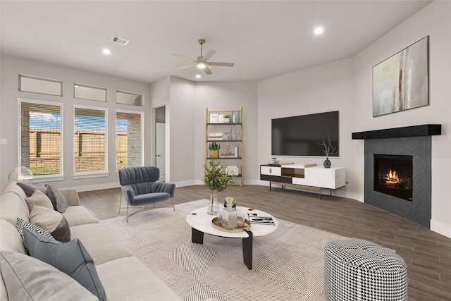 living room with hardwood / wood-style flooring, ceiling fan, and a tiled fireplace