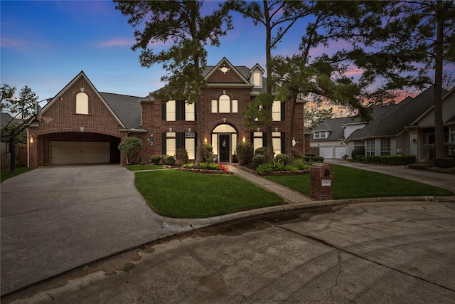 colonial house with a garage, a lawn, concrete driveway, and brick siding