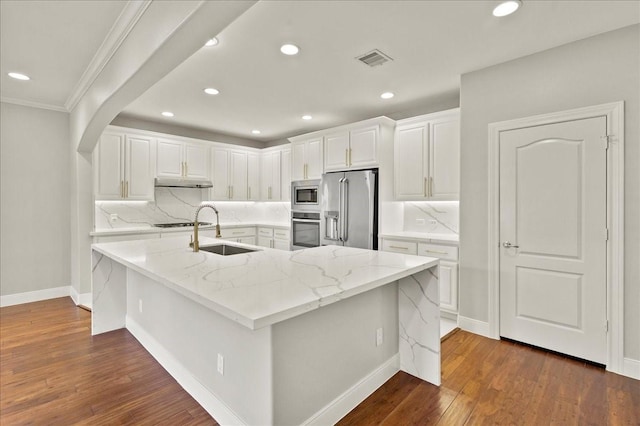 kitchen with light stone countertops, stainless steel appliances, sink, a center island with sink, and white cabinets