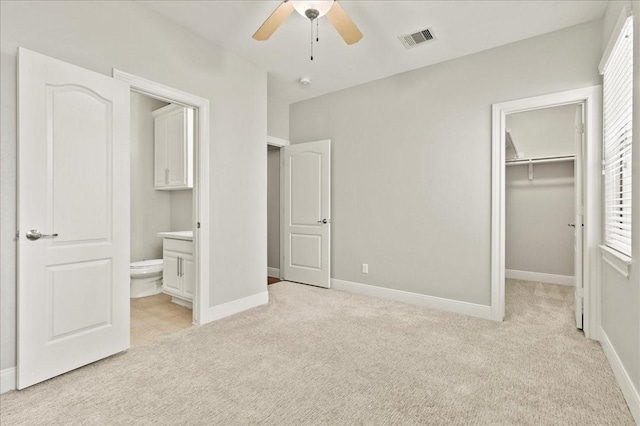 unfurnished bedroom with connected bathroom, a spacious closet, ceiling fan, light carpet, and a closet