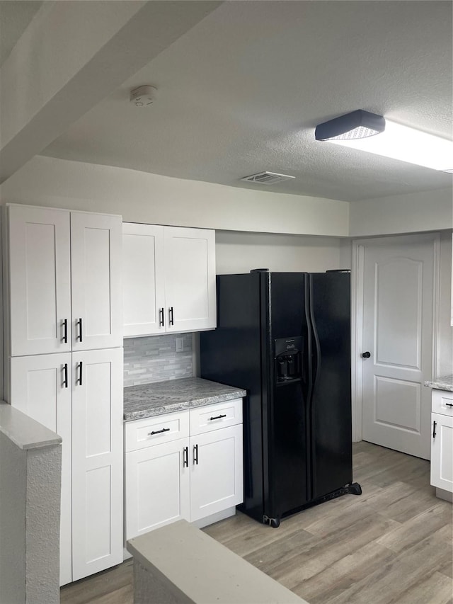 kitchen with backsplash, black refrigerator with ice dispenser, white cabinets, and light hardwood / wood-style floors