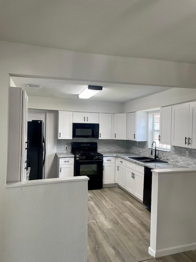 kitchen featuring sink, light hardwood / wood-style flooring, backsplash, white cabinets, and black appliances