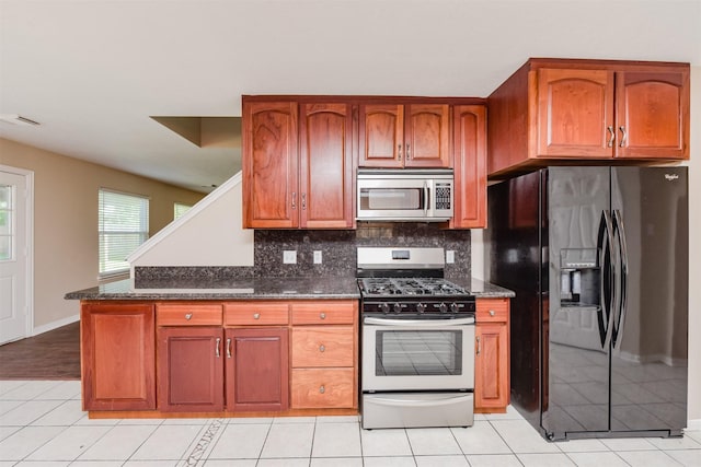 kitchen with backsplash, black fridge, range with gas cooktop, light tile patterned floors, and dark stone countertops