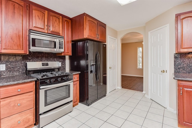 kitchen featuring tasteful backsplash, light tile patterned floors, dark stone counters, and appliances with stainless steel finishes