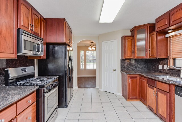 kitchen with appliances with stainless steel finishes, backsplash, dark stone counters, ceiling fan, and sink