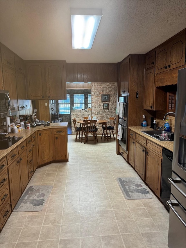 kitchen with sink, appliances with stainless steel finishes, light tile patterned flooring, kitchen peninsula, and brick wall