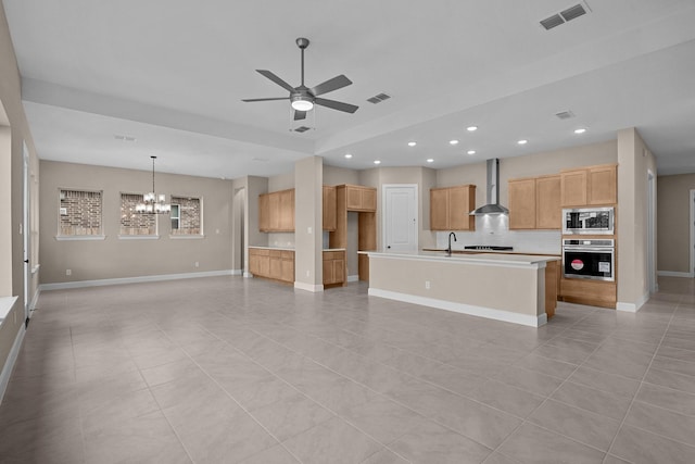 kitchen with light tile patterned floors, stainless steel appliances, a kitchen island with sink, and wall chimney exhaust hood