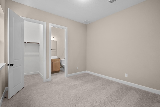 unfurnished bedroom with light carpet, a closet, ensuite bath, and a spacious closet